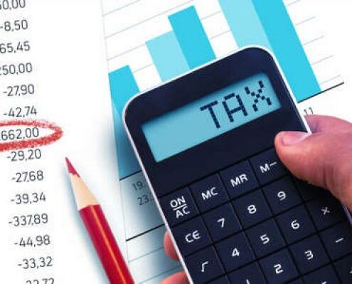 A calculator spells out the word tax over a piece of paper with a bar graph on it